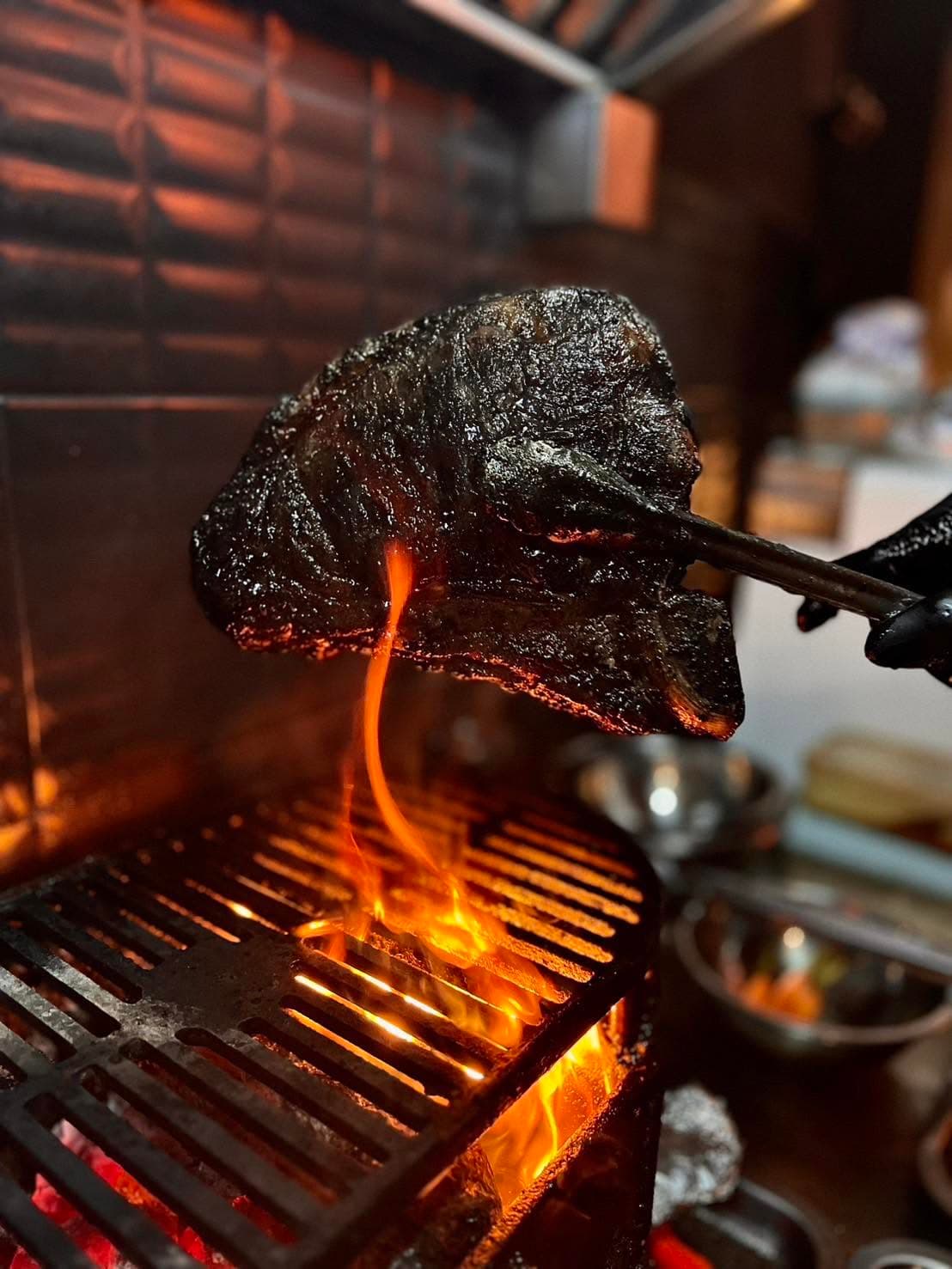 A steak held in tongs over open flame at Ob'serve