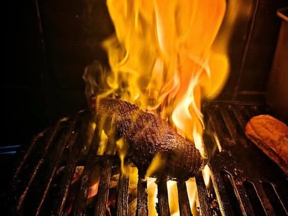 Flames leaping around meat on the charcoal grill at Ob'serve