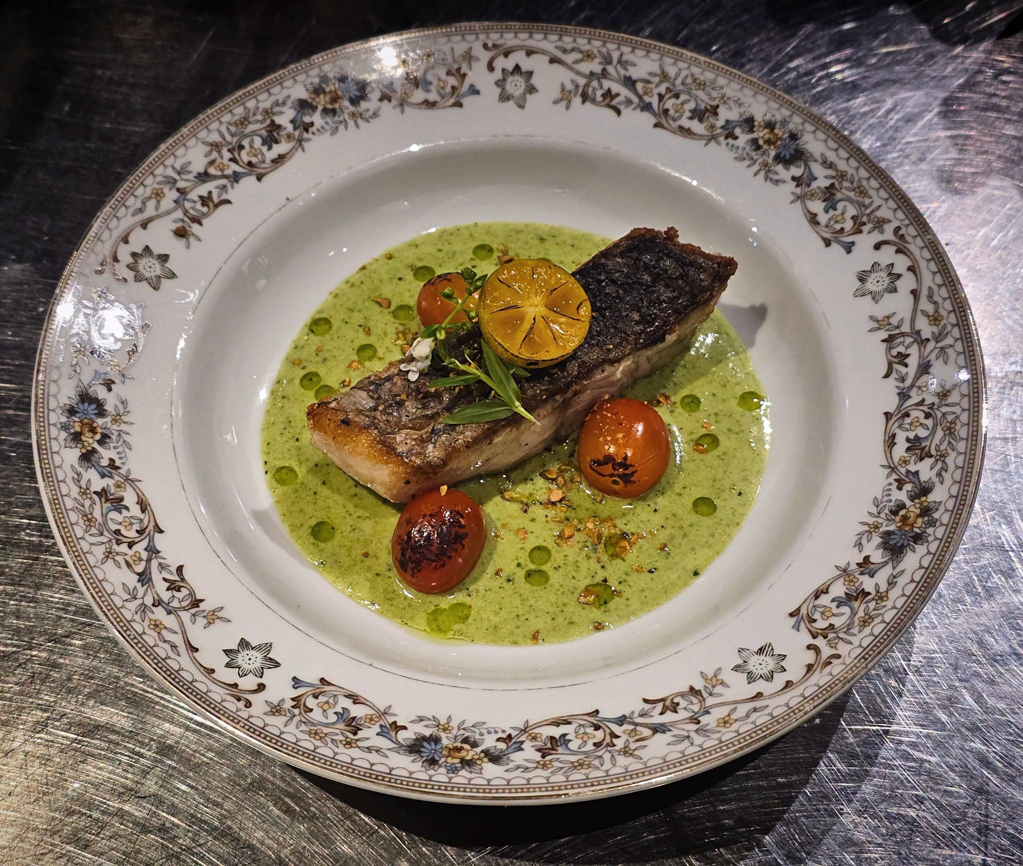 Crisp-skinned fish in bright herb sauce with blistered tomatoes, plated on vintage china at Ob'serve